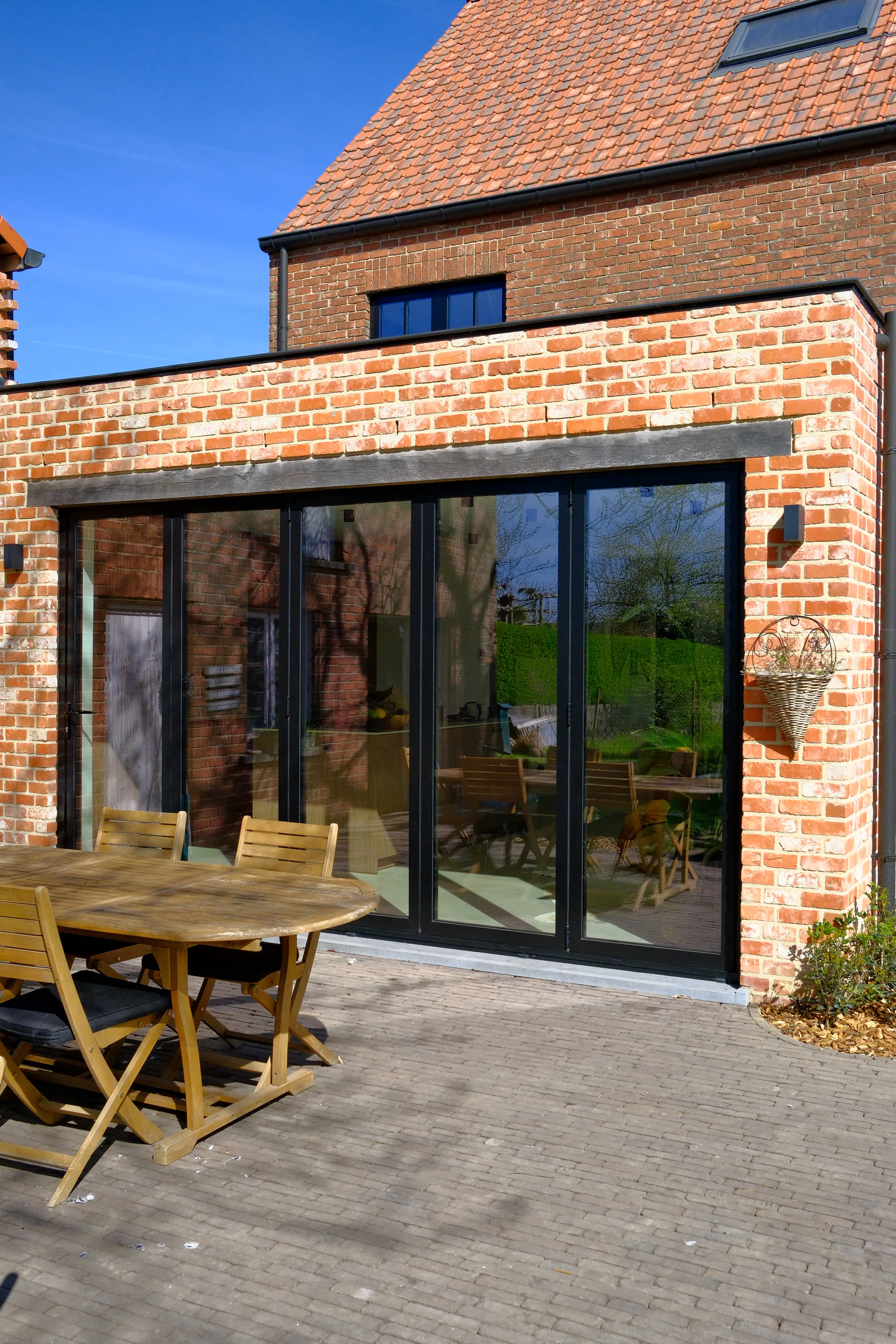 Bakstenen uitbouw met vouwdeuren, harmonica raam en terras met houten tafel — totaalproject BVDH · West-Vlaanderen door BVDH