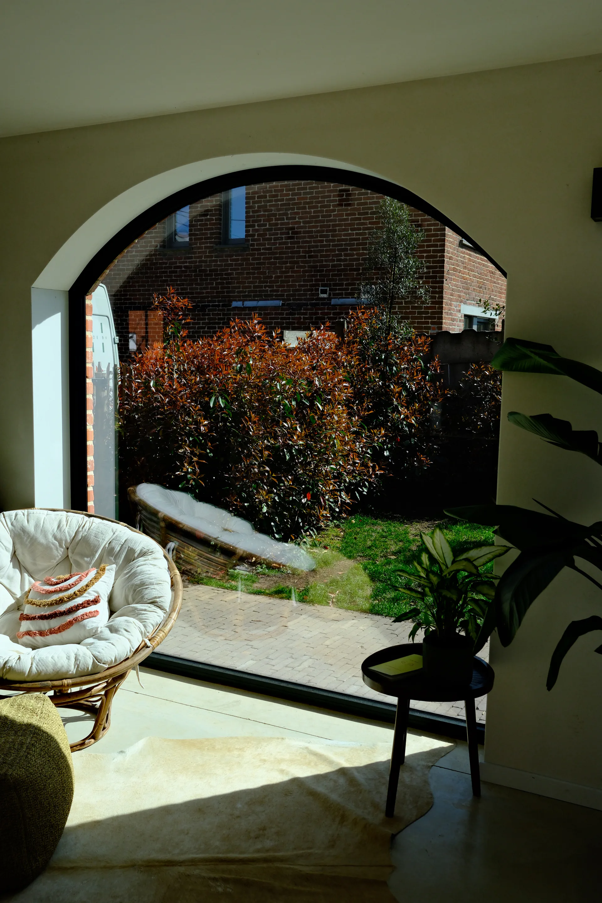 Woonkamer met groot boograam en tuinzicht, papasan stoel en natuurlijk licht — maatwerk interieur BVDH · West-Vlaanderen door BVDH
